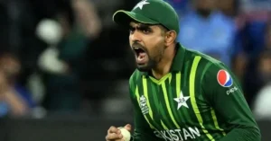 Cricketer in a green jersey celebrating passionately, holding a cricket ball in his hand, with a determined expression. The background features a blurred stadium setting.